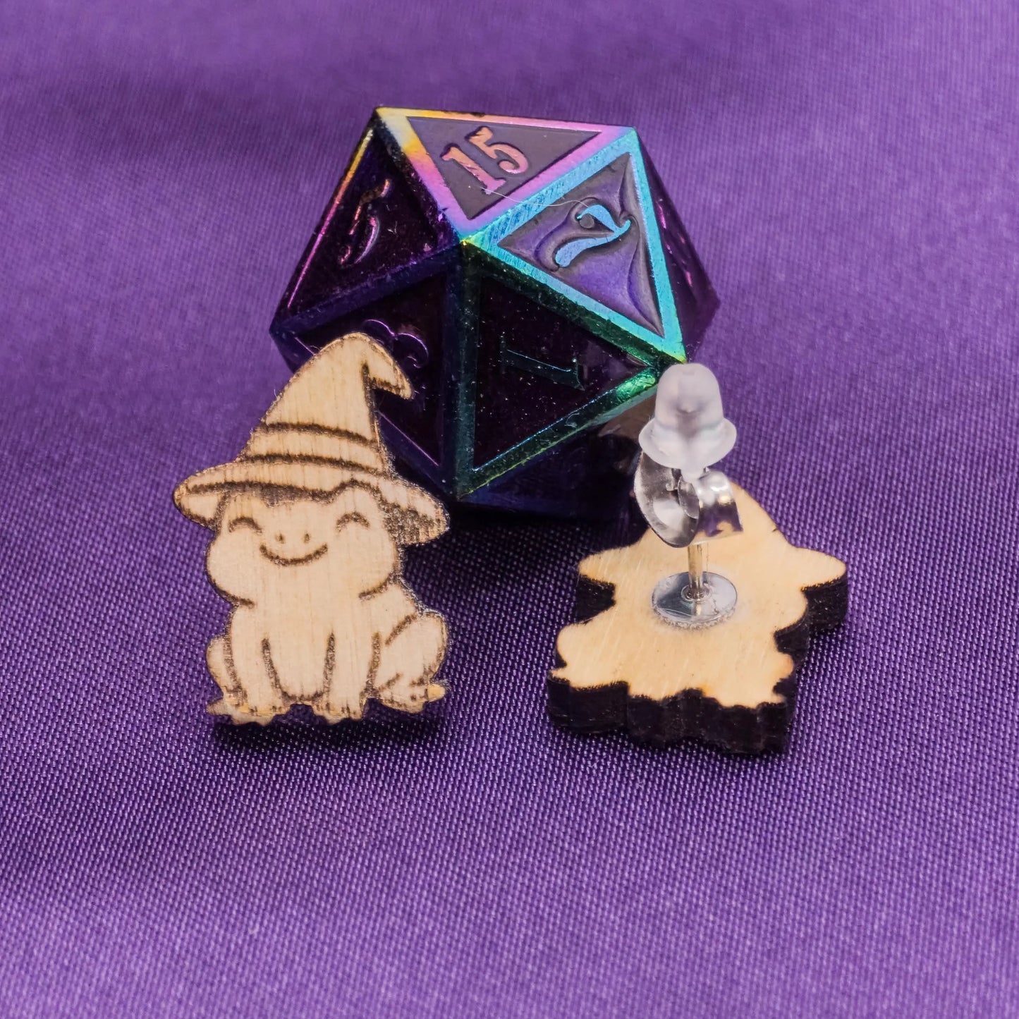 D20 polyhedral dice with small wooden laser engraved frog earrings on a purple background