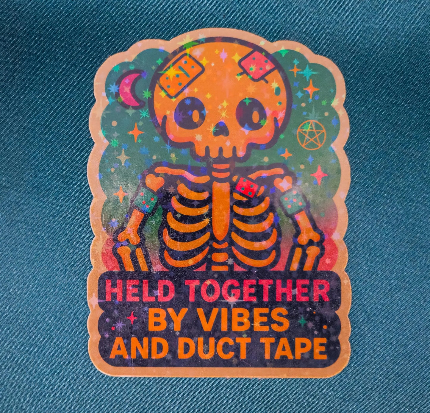 Colorful skeleton sticker with text 'HELD TOGETHER BY VIBES AND DUCT TAPE' on a blue background
