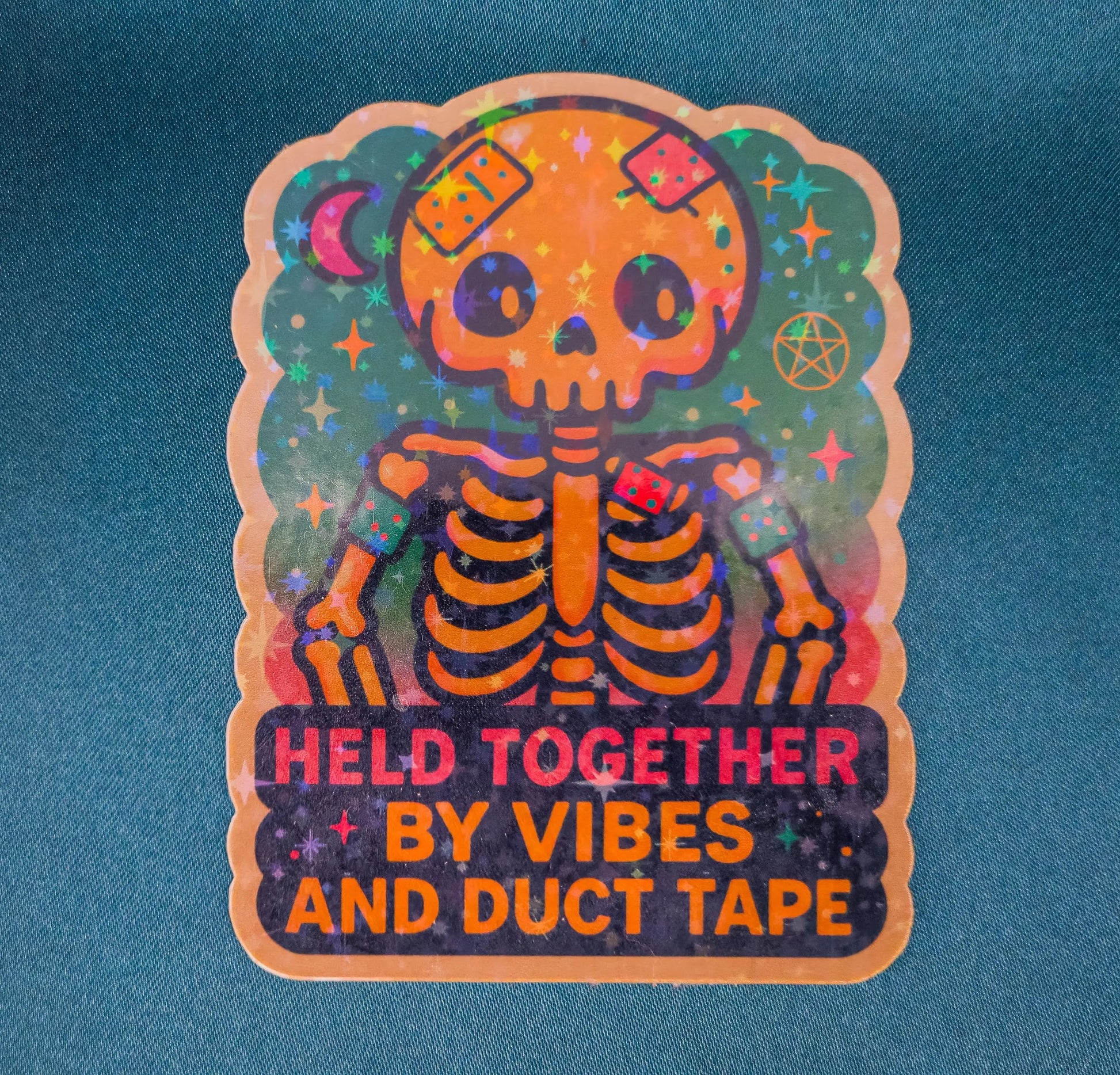 Colorful skeleton sticker with text 'HELD TOGETHER BY VIBES AND DUCT TAPE' on a blue background