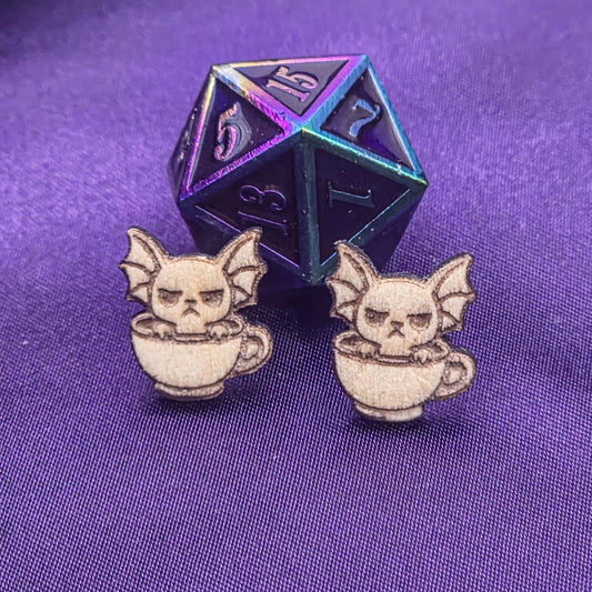 Pair of laser engraved earrings featuring bats sitting in a teacup with a D20 dice on a purple background