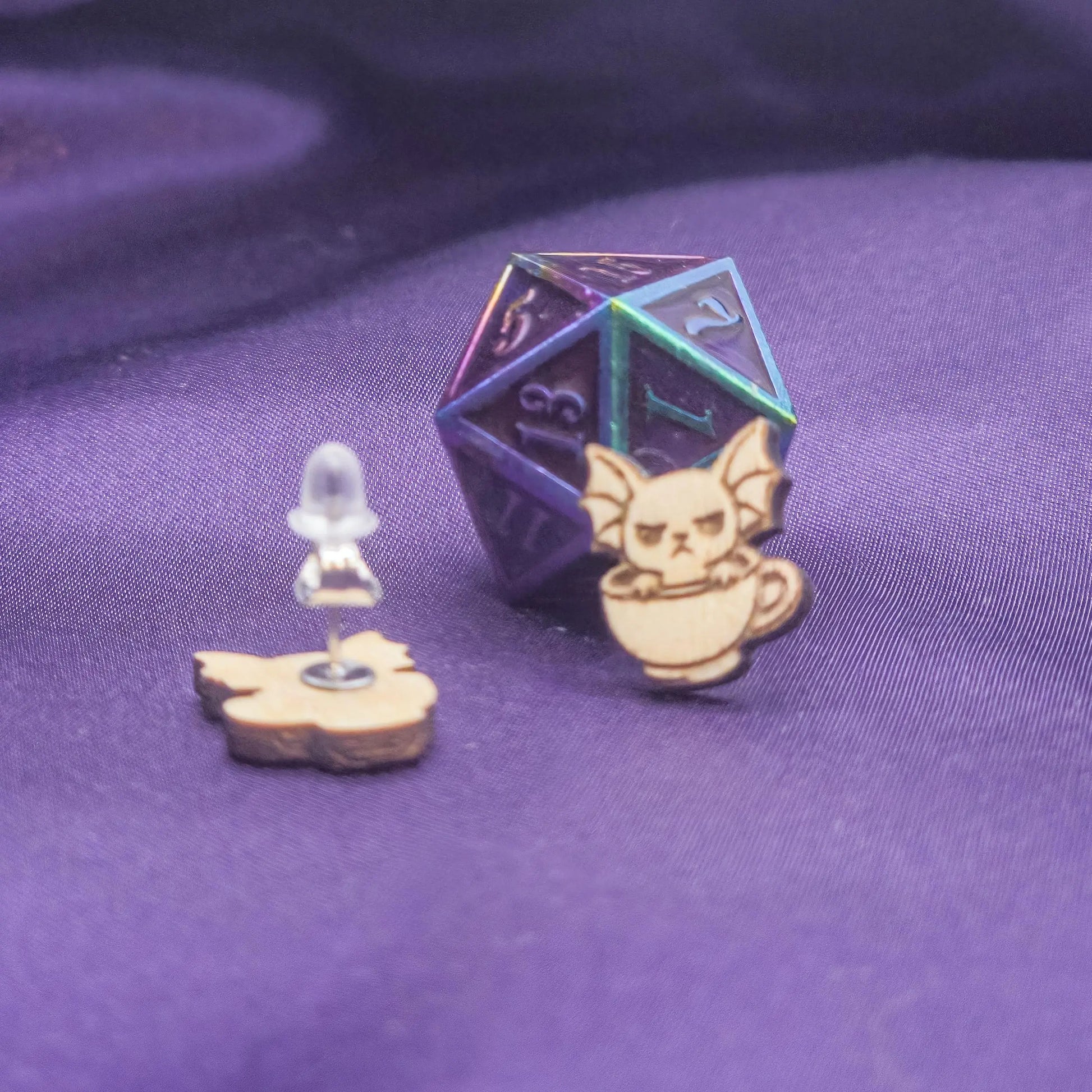 Pair of laser engraved earrings featuring bats sitting in a teacup with a D20 dice on a purple background