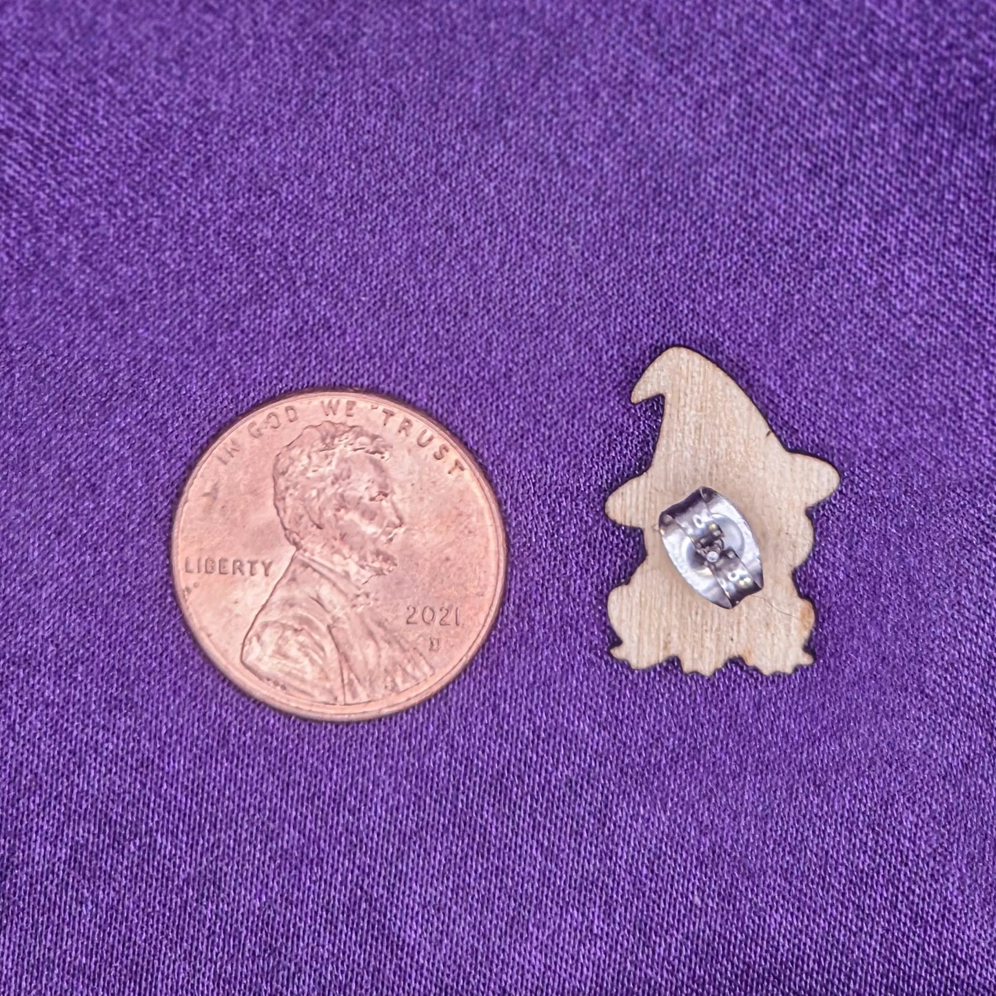 backside of earring on a purple fabric background, next to a penny for scale.