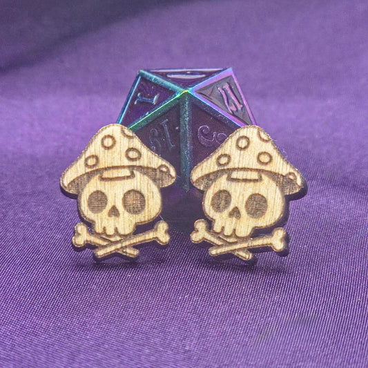 Skull and mushroom earrings with a metallic die on a purple fabric background