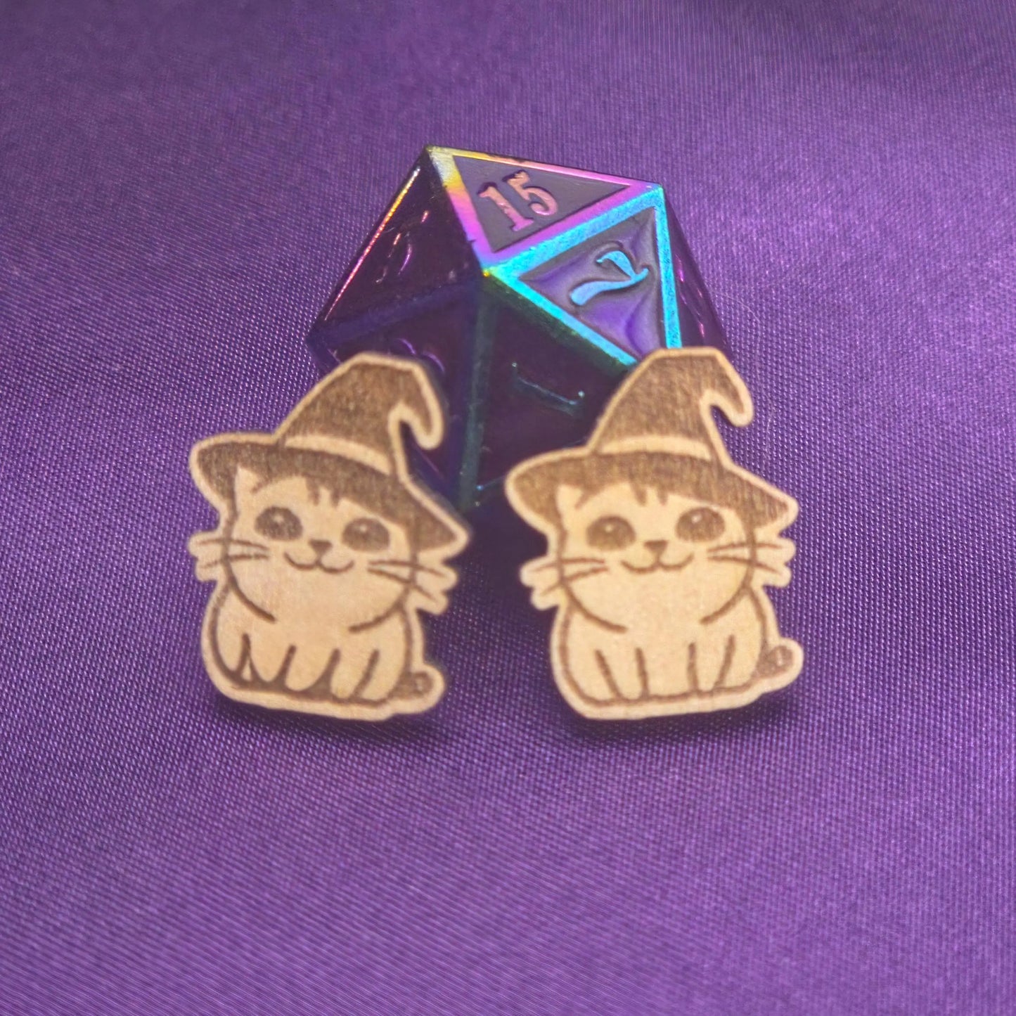 a pair of laser engraved earrings featuring cats in witch hats in front of a d20