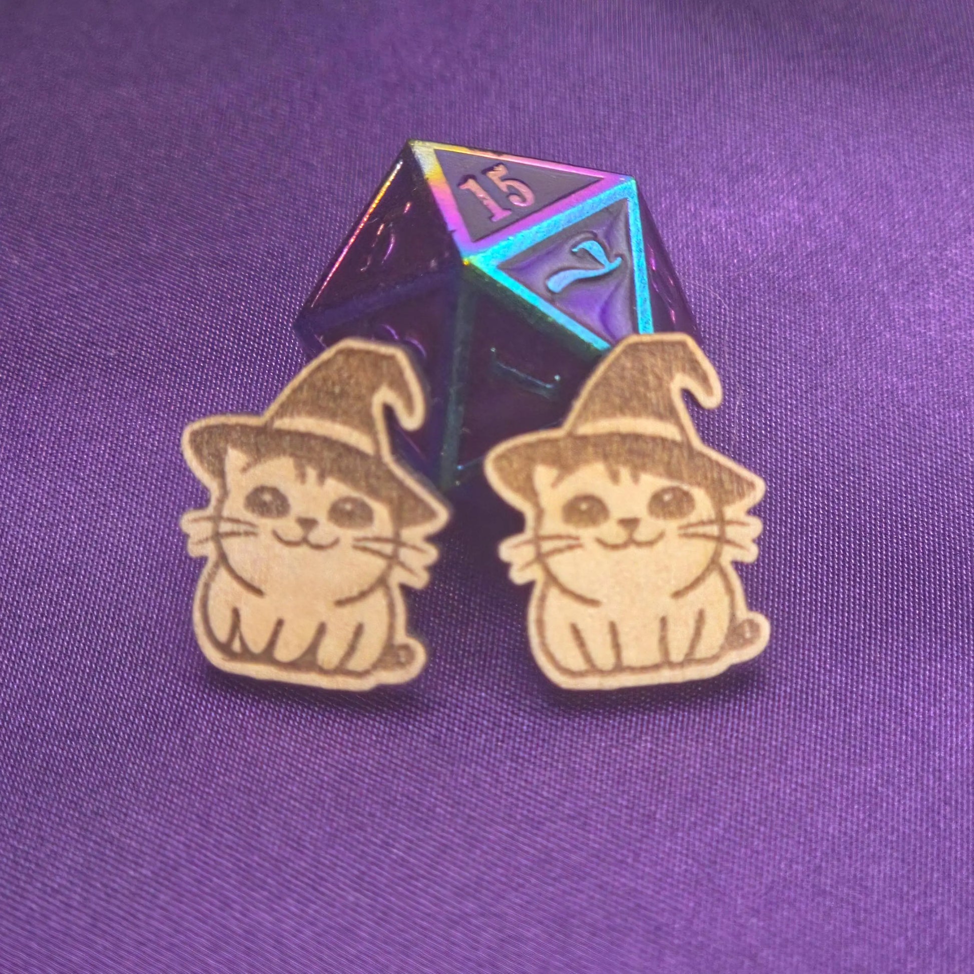 a pair of laser engraved earrings featuring cats in witch hats in front of a d20