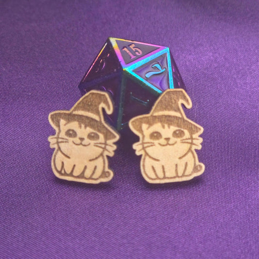 a pair of laser engraved earrings featuring cats in witch hats in front of a d20
