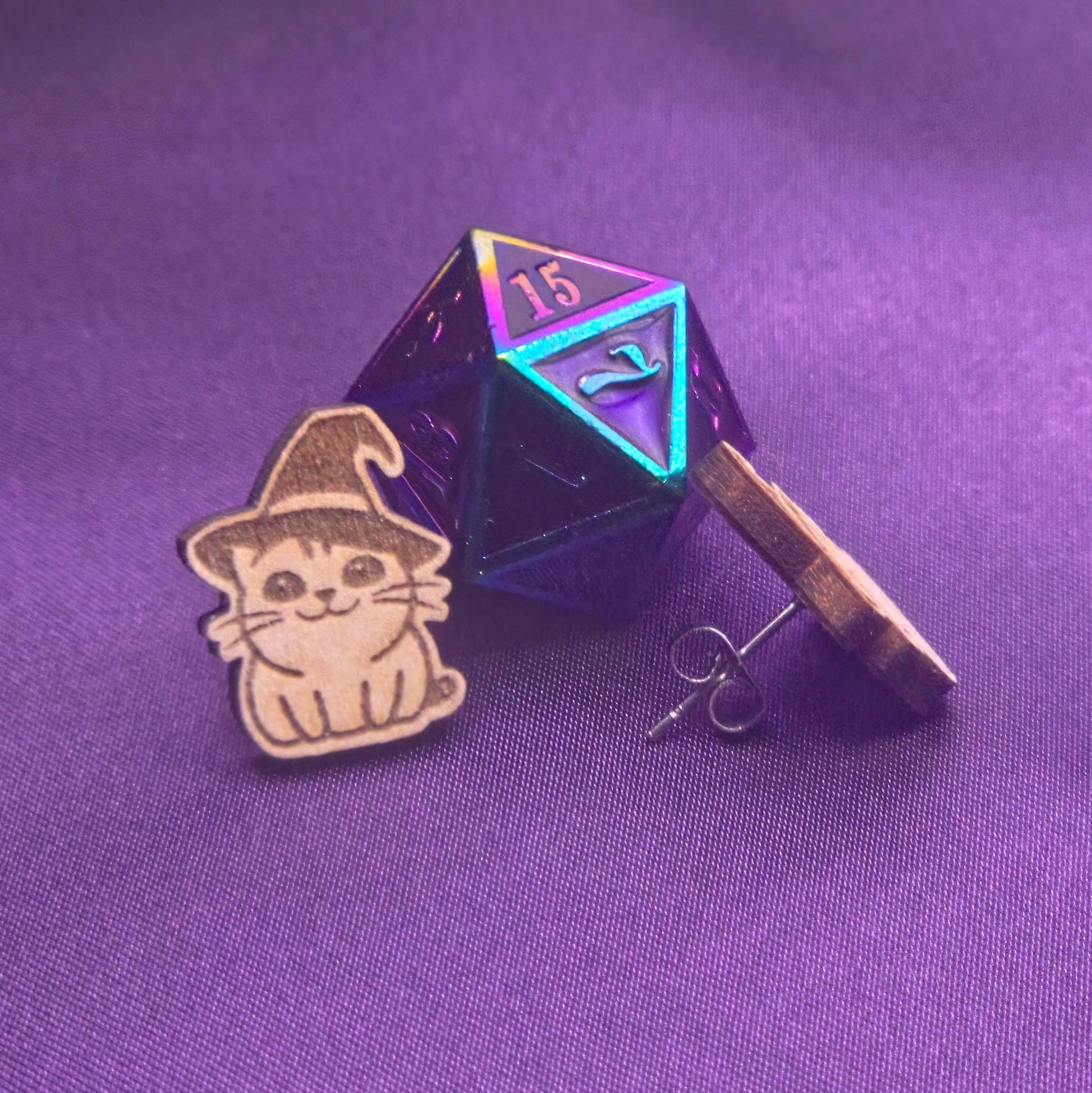 laser engraved earring featuring a cat with a witchy hat next to a metal polyhedral die on a purple background