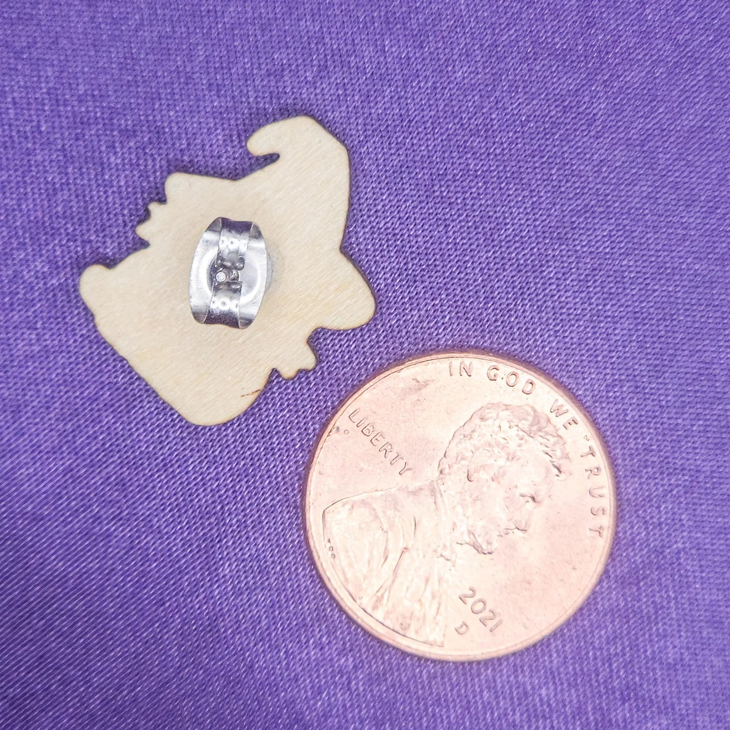 backside view of a laser engraved earring with a penny for scale on a purple background