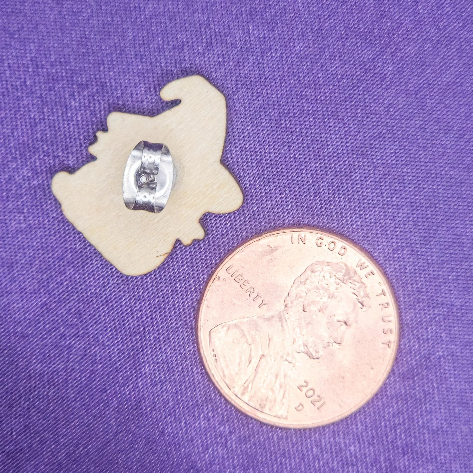backside view of a laser engraved earring with a penny for scale on a purple background