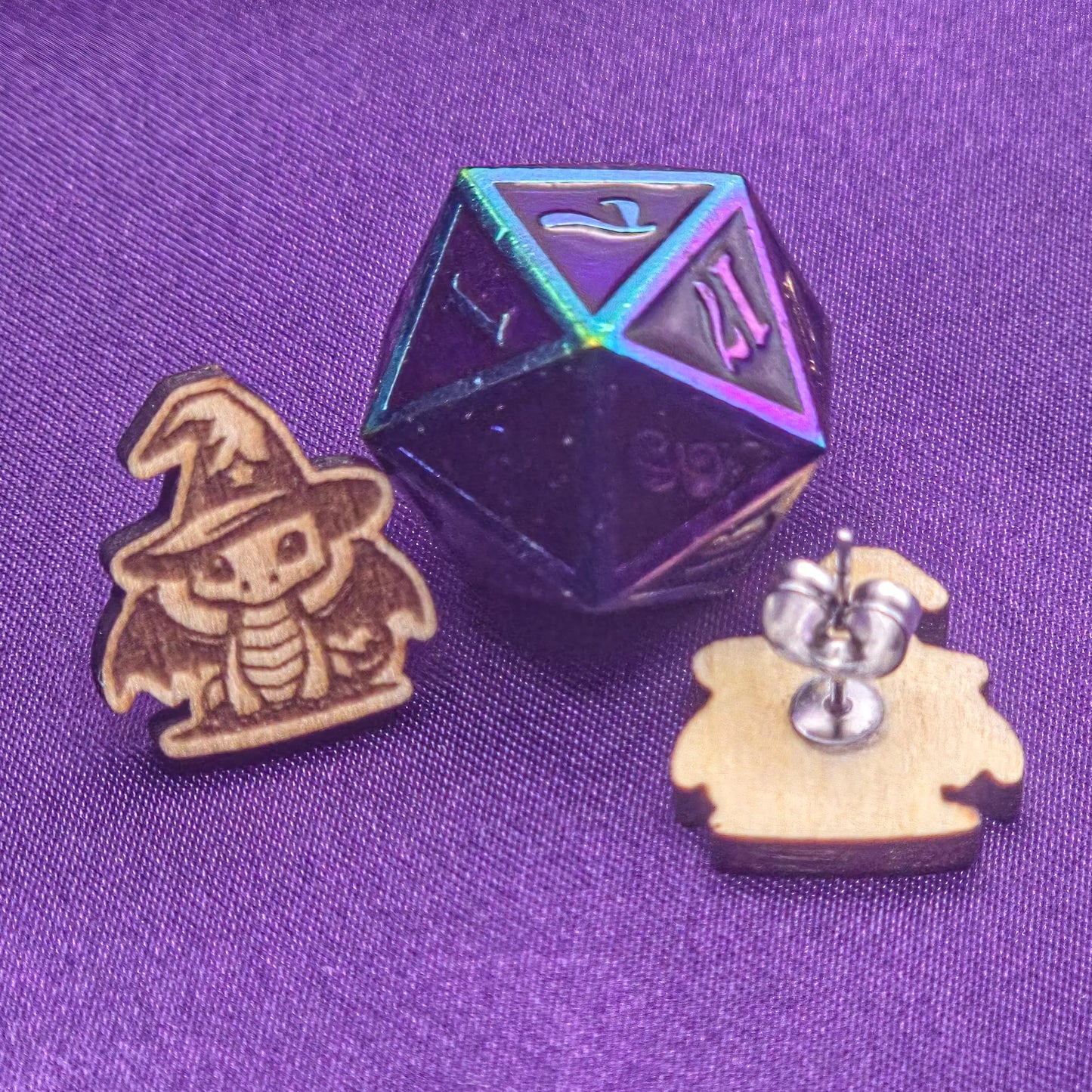 Wooden dragon-shaped earrings with a metallic die on a purple fabric background