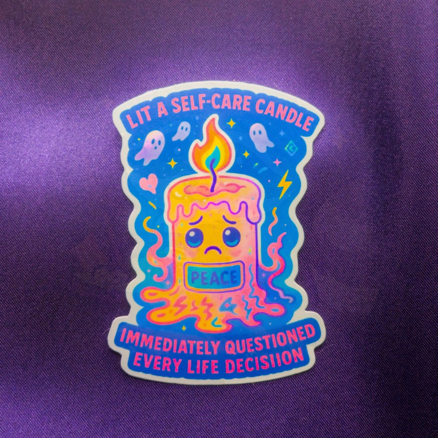 Sticker on purple fabric shows a sad, melting candle labeled "Peace." Surrounding text reads: "Lit a self-care candle, immediately questioned every life decision." Fun, whimsical style.