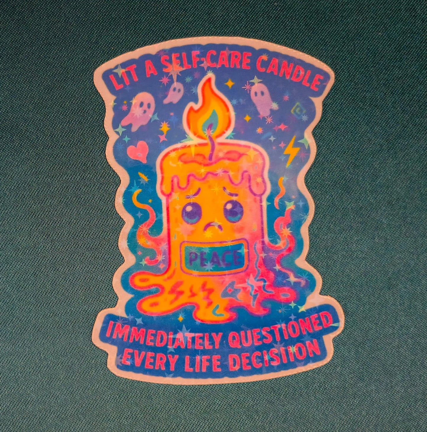 Illustrated candle with a sad face labeled "Peace" melts with colorful drips. Surrounded by ghosts and stars, caption reads "Lit a self-care candle, immediately questioned every life decision."