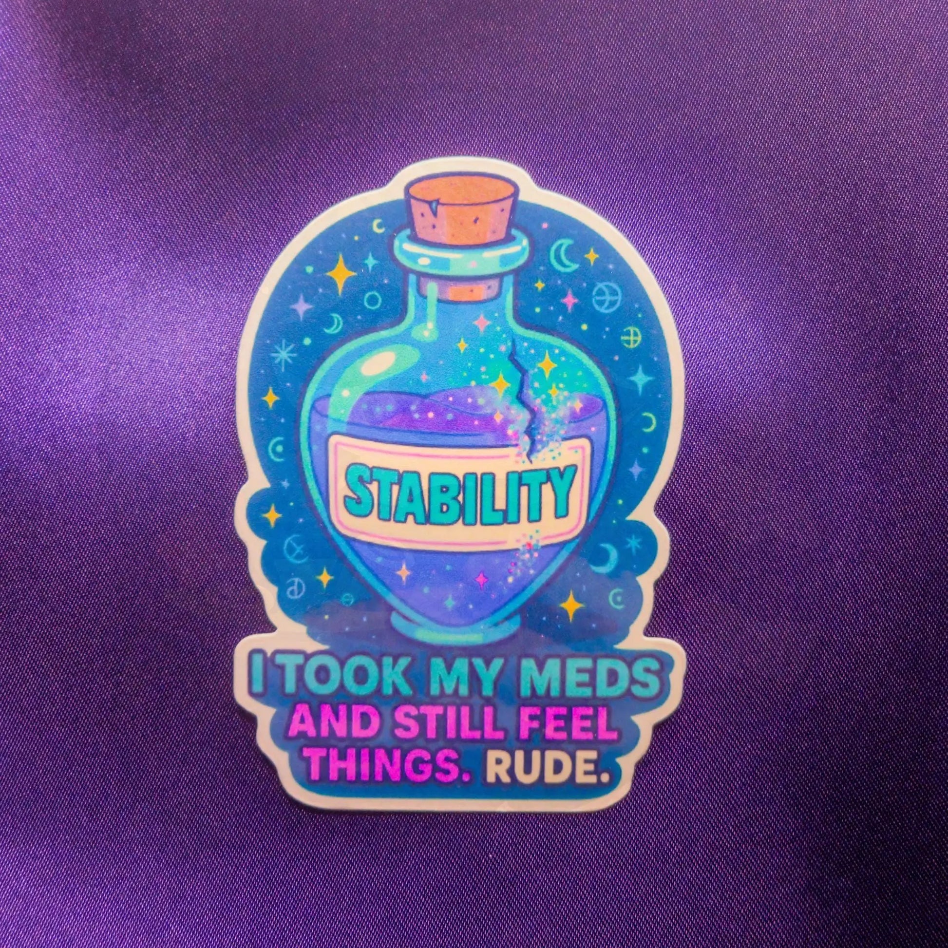A sticker on a purple background shows a magical potion bottle labeled "Stability" with stars and planets. Text below reads, "I took my meds and still feel things. Rude." The tone is humorous.